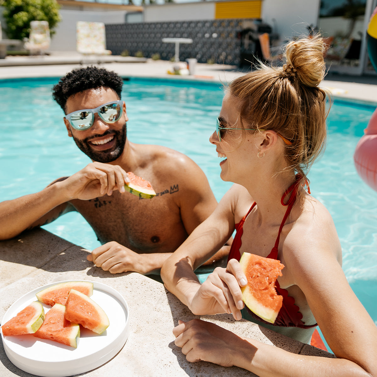Couple eating watermelon by the pool wearing Knockaround sunglasses