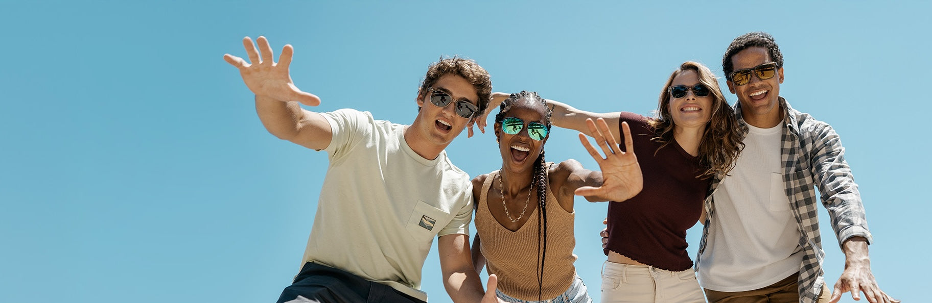 Four friends posing together wearing Knockaround sunglasses against a clear blue sky
