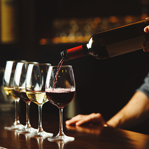 Bartender pours red wine in glasses on wooden bar counter