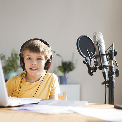 Young boy listening with headphones next to podcast equipment