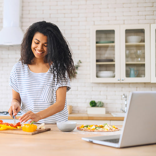 Young woman chopping peppers while watching cooking class on a laptop