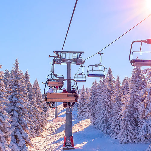 Skiers on a chairlift surrounded by white snow pine trees