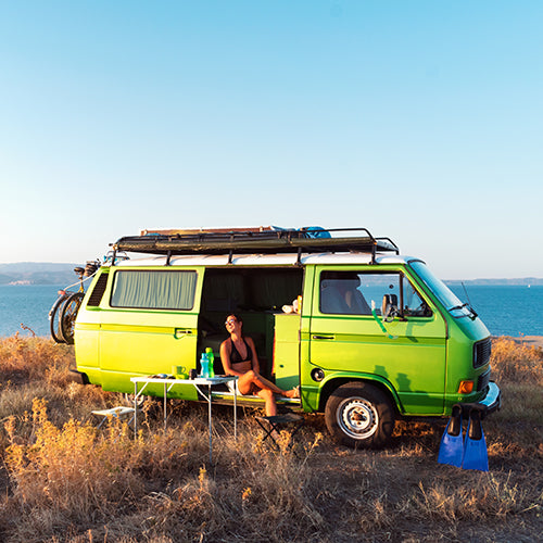 Female sitting in a green campervan near the ocean