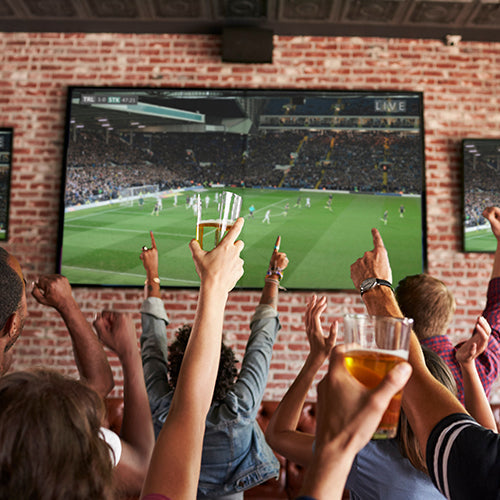 Rear View Of Friends Watching Game In Sports Bar On Screens