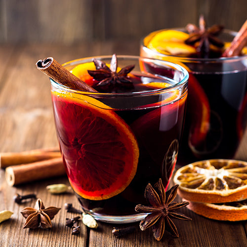Two glasses of mulled wine with oranges and spices on wooden background