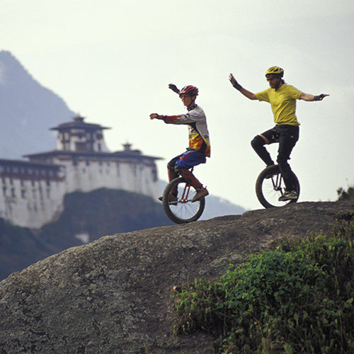 Two unicyclists riding down a hill