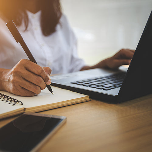 Woman taking notes while learning online with laptop