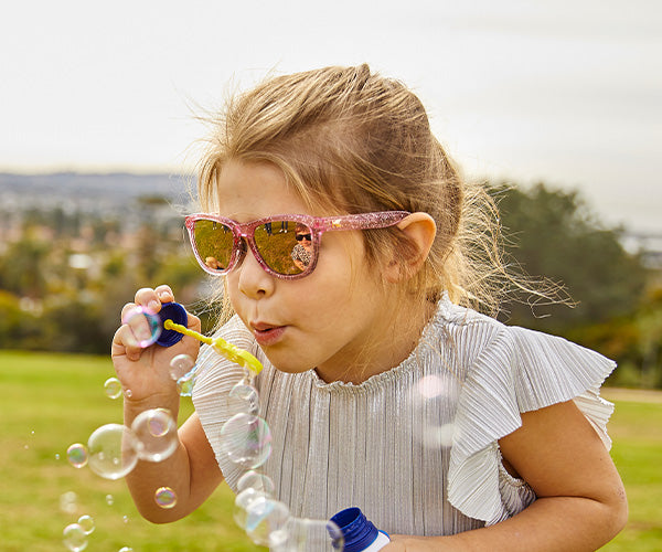 Child blowing bubbles wearing Pink Sparkle Kids Premiums sunglasses