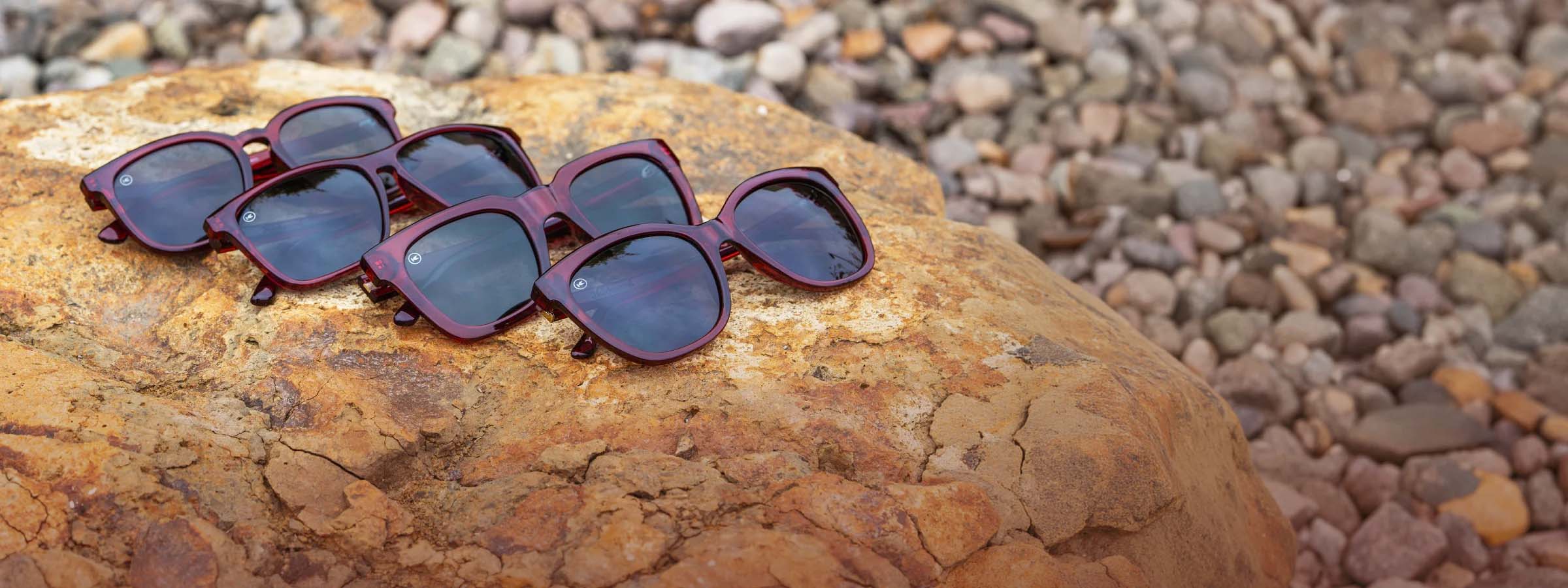4 Black Cherry burgundy translucent sunglasses photographed on a rock