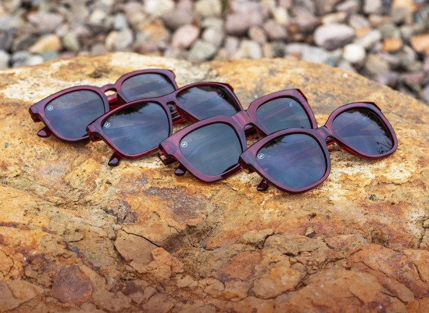 4 Black Cherry burgundy translucent sunglasses photographed on a rock