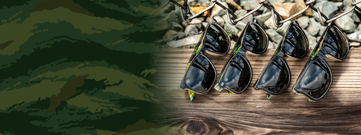 Covert Ops sunglasses. 4 pairs of black and camo print sunglasses with smoke lenses photographed on a wood in nature