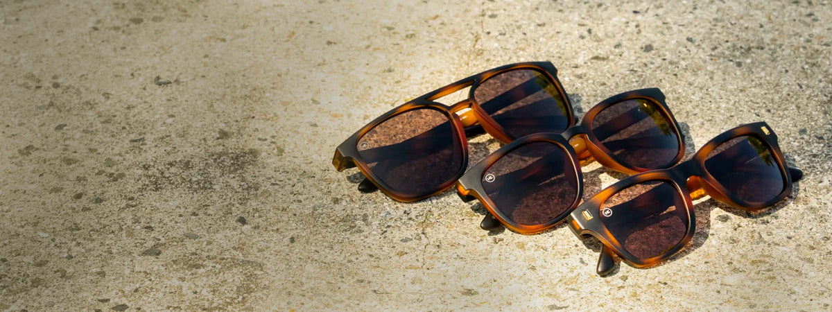 Three pairs of tortoise shell Cypress sunglasses with amber lenses arranged diagonally on a textured concrete surface.