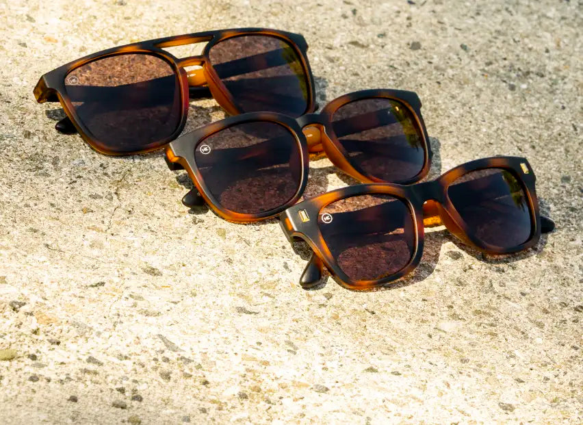 Three pairs of tortoise shell Cypress sunglasses with amber lenses arranged diagonally on a textured concrete surface.
