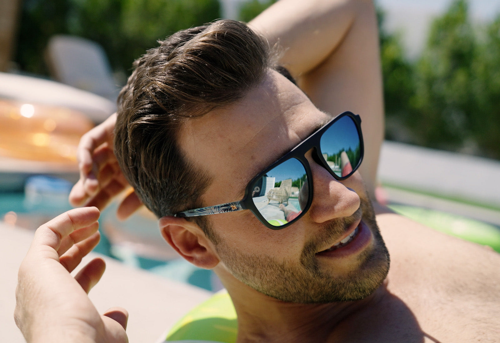 Sunglasses with black fronts, blue palm tree arms and polarized sky blue lenses, model