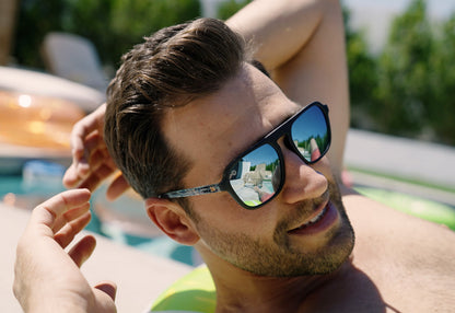 Sunglasses with black fronts, blue palm tree arms and polarized sky blue lenses, model