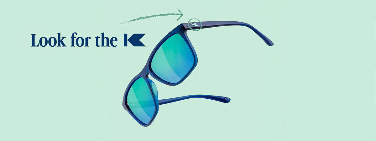 Navy / Mint Fast Lanes Sport sunglasses photographed on a light blue background with "Look for the K" text overlayed and an arrow pointing to the K logo on the sunglasses