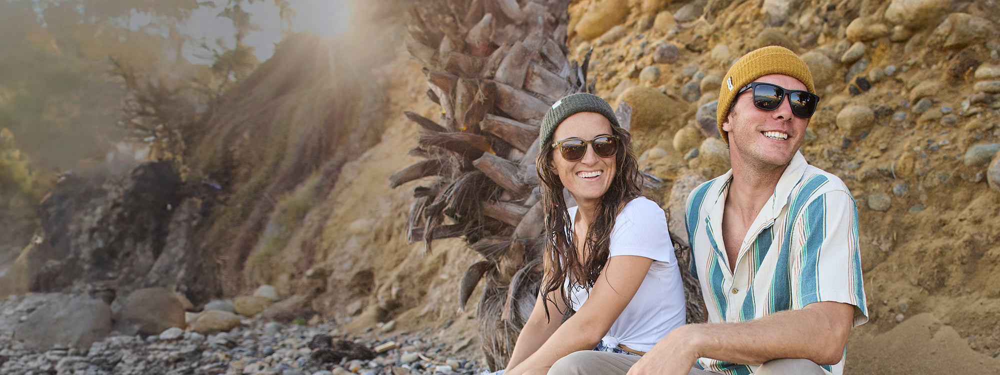 Two people sitting on a rocky beach wearing Knockaround sunglasses.