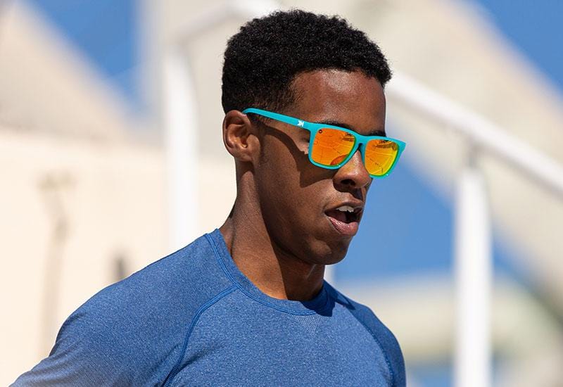 Male model wearing sport sunglasses with Pool Blue Frames and Polarized Orange Sunset Lenses